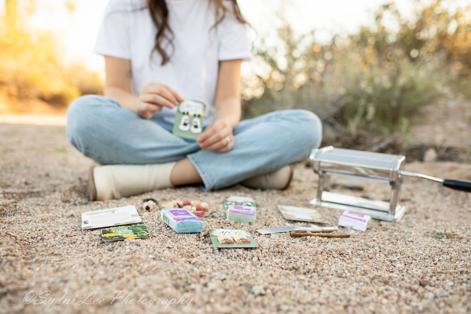 Person sitting on ground with craft supplies scattered around in warm outdoor setting.