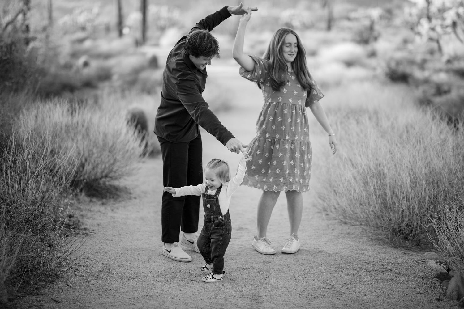 Black and white photo of children walking hand in hand down a winding desert path with brush on either side.