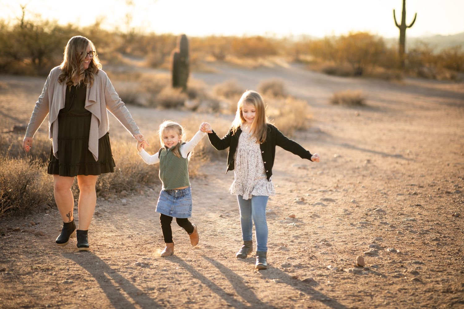 A family walks together on a desert trail at sunset with tall saguaro cacti in the background at Lost Dutchman state park.