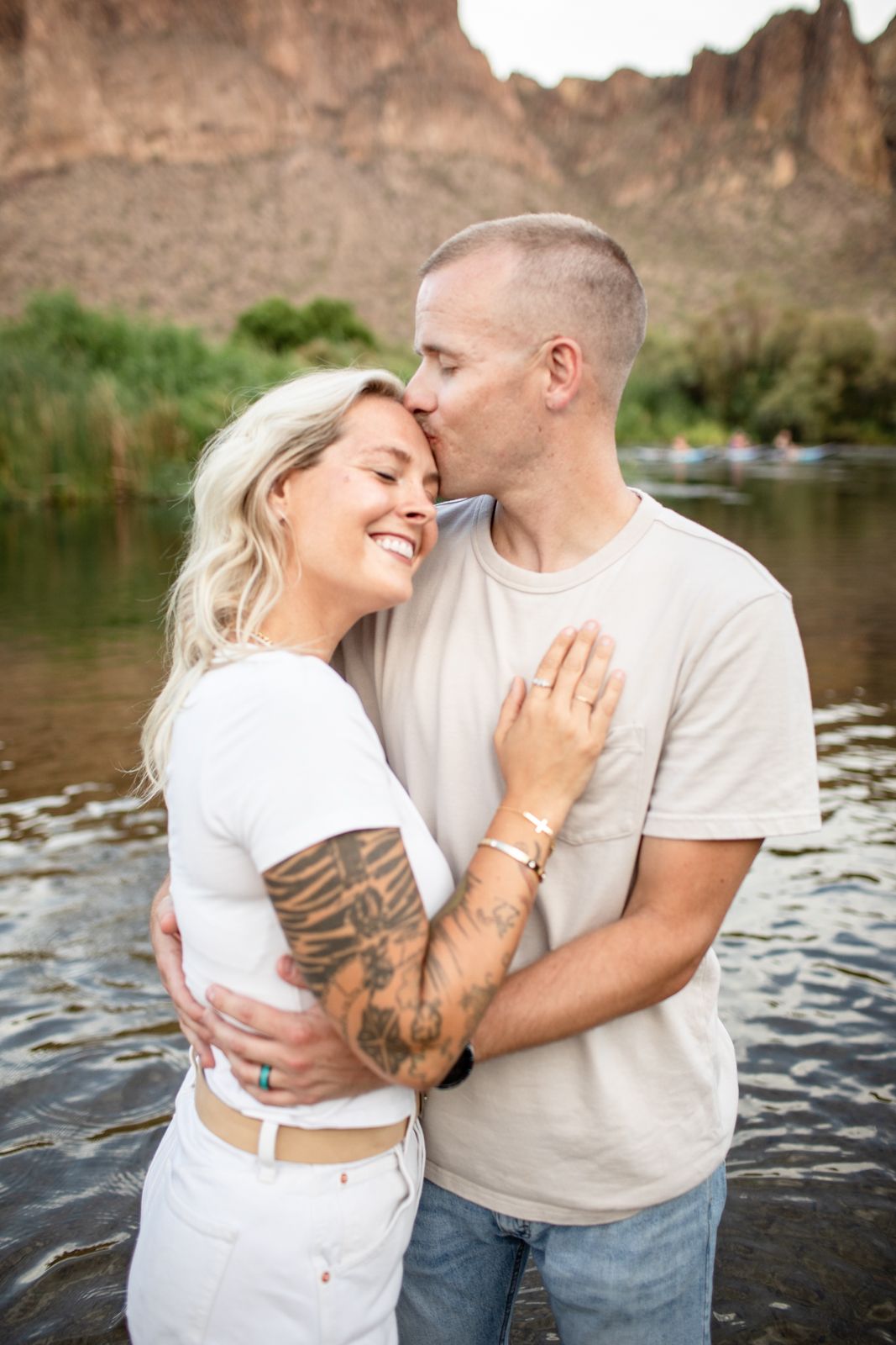 Couple in white shirts sharing intimate moments by a river during a romantic outdoor photoshoot at Water Users recreational area.