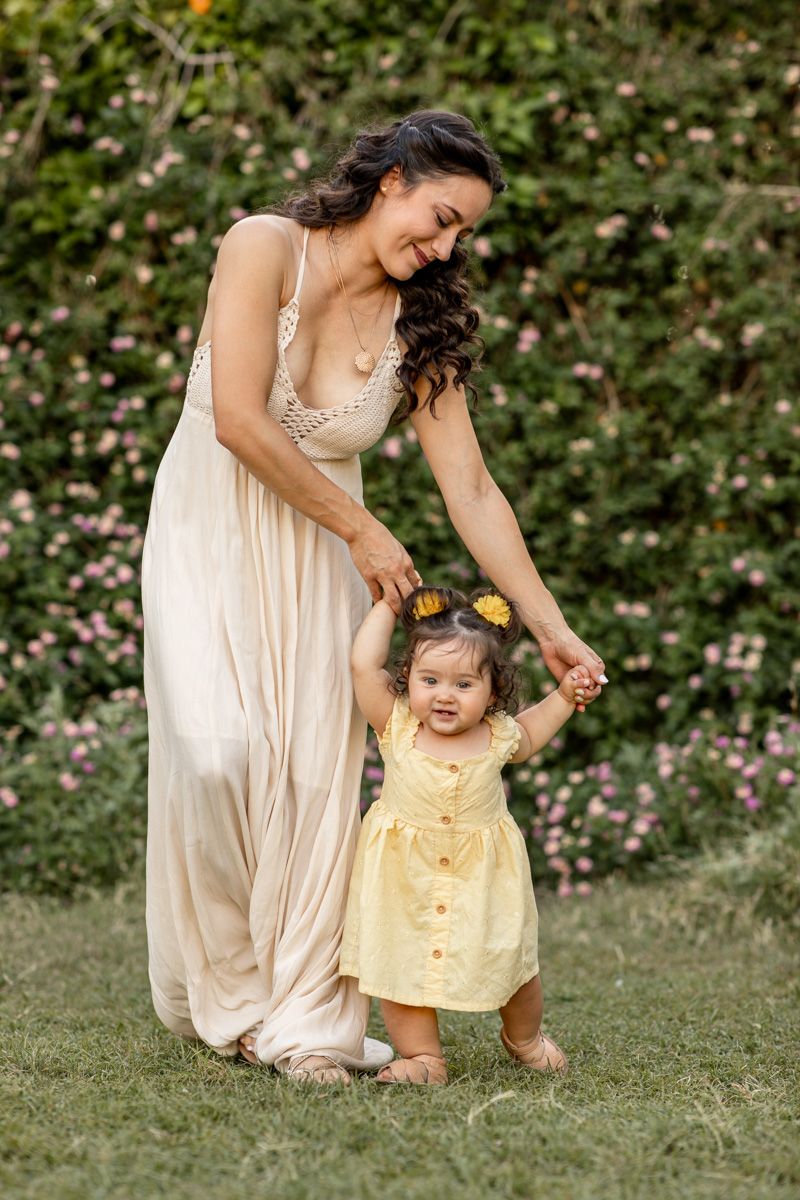 A parent and child in flowing dresses share a joyful moment playing together in a garden setting.