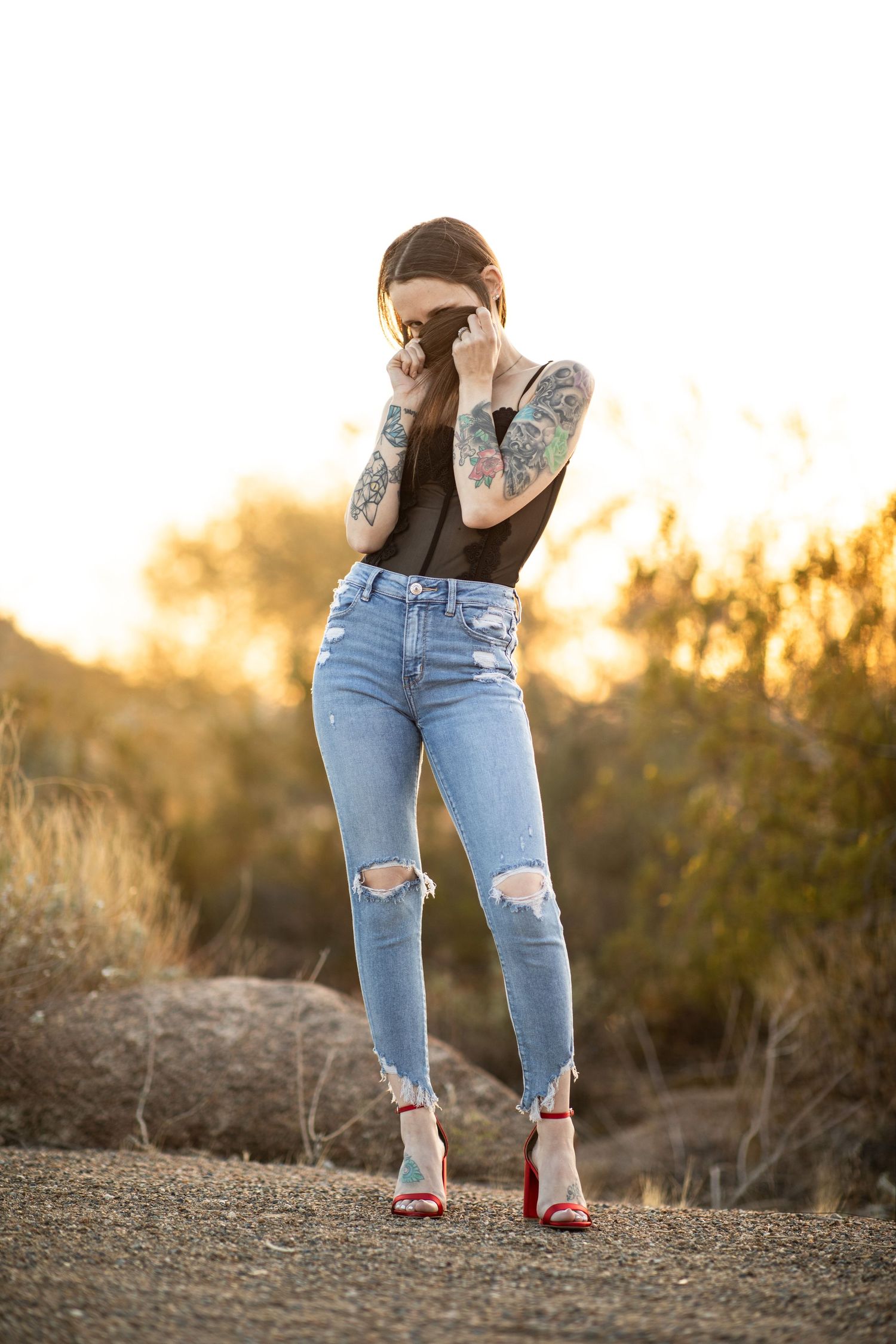 Person wearing ripped blue jeans and red heels stands on rocky desert terrain at sunset at Desert Arroyo park in Mesa, AZ.