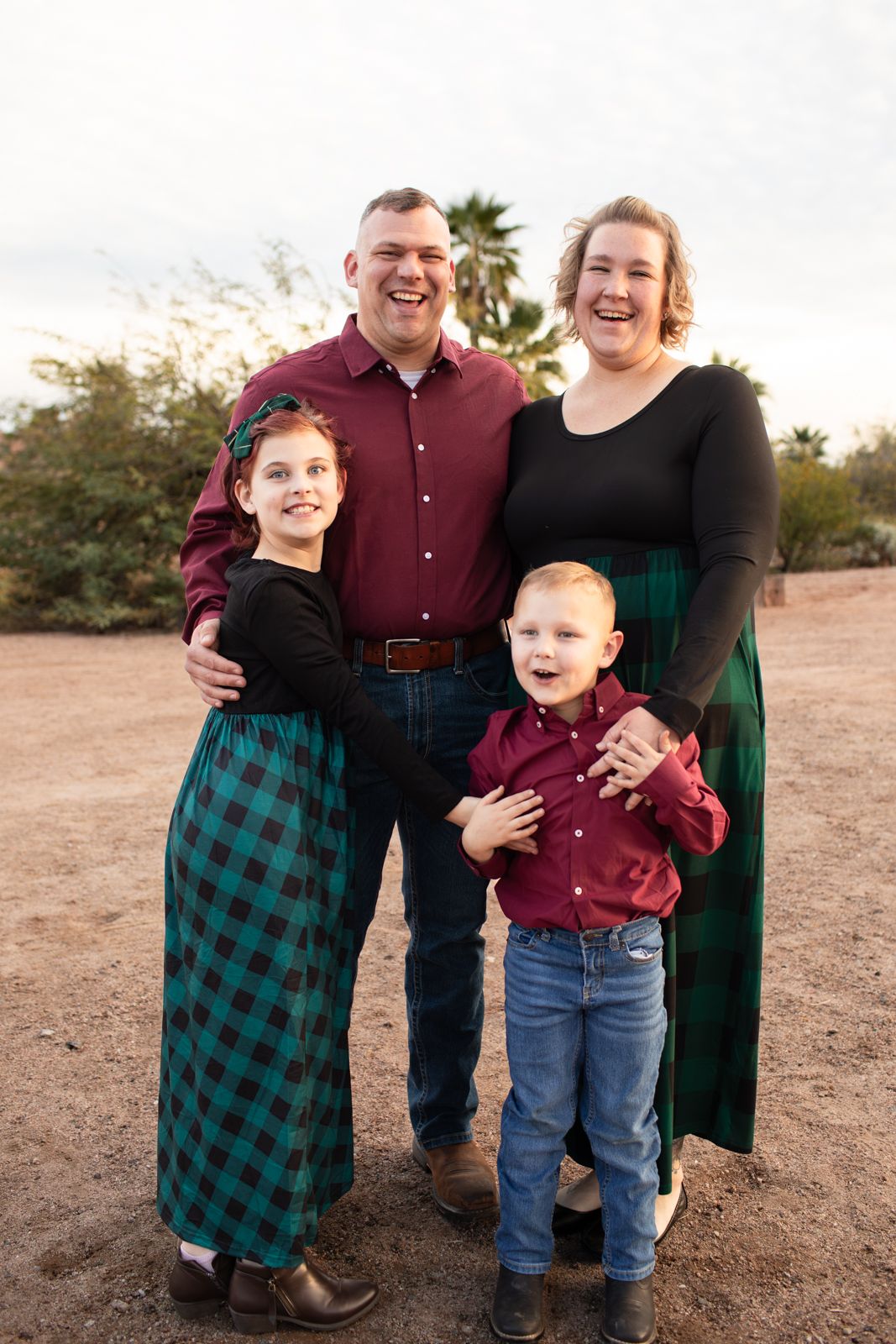 Family group poses in coordinated holiday outfits with green plaid and burgundy colors in Papago Park in Phoenix, AZ.