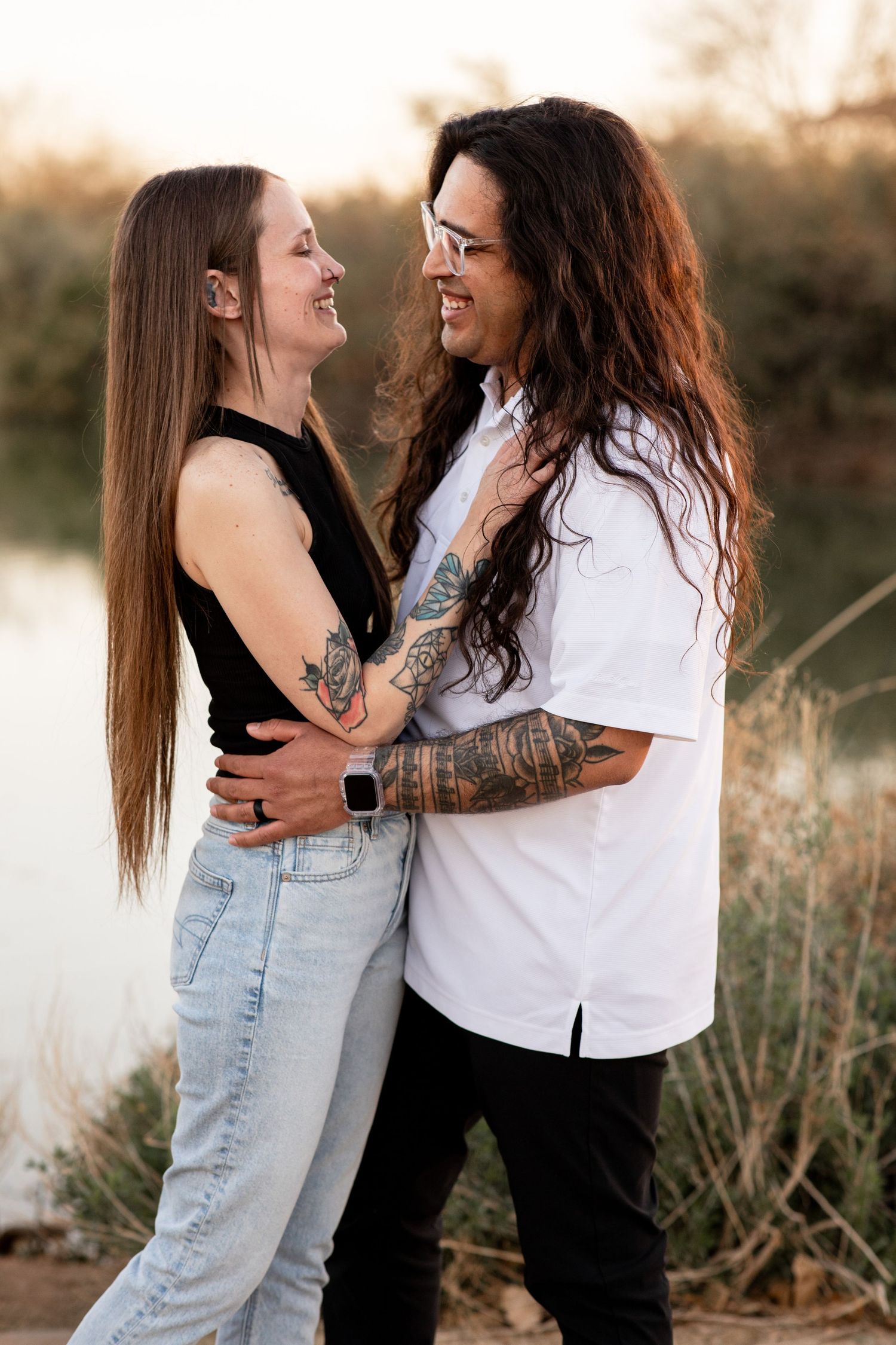 A romantic couple embraces outdoors during golden hour in a natural setting with tall grass and warm lighting.