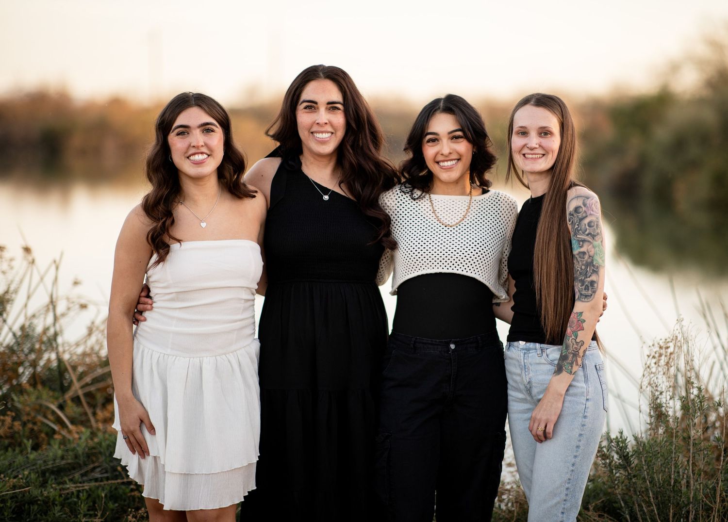 A group stands together outdoors at sunset with golden light filtering through tall grass and trees in the background.