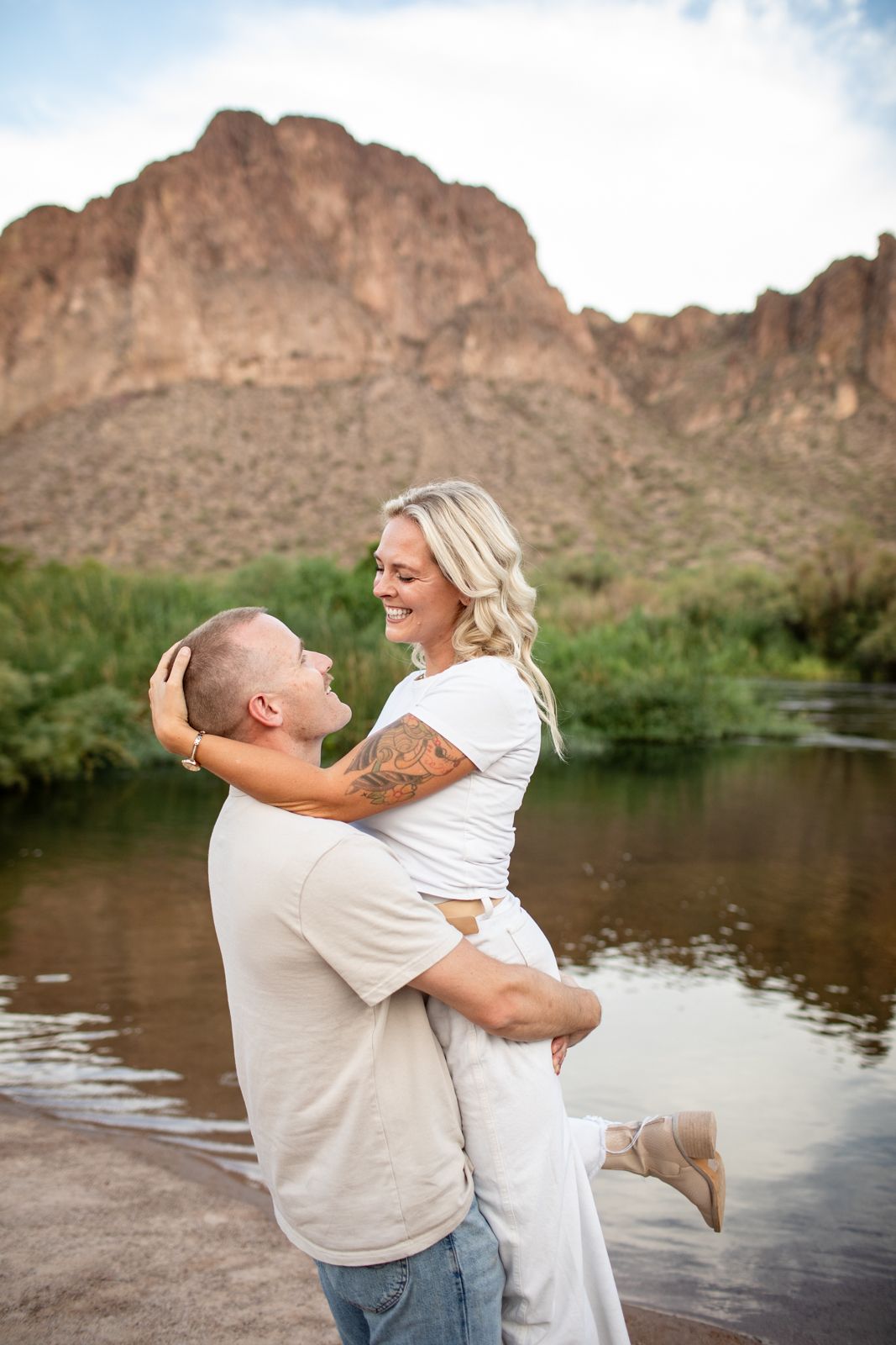 Couple shares a joyful embrace by a scenic lake with rugged mountain cliffs in the background at Water Users recreational area.