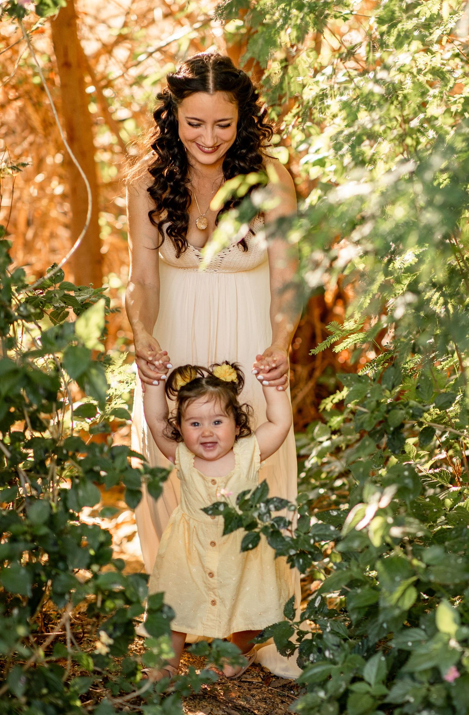 A mother and toddler share a tender moment among sunlit trees and leaves in a natural outdoor setting at The Meadow in Mesa.
