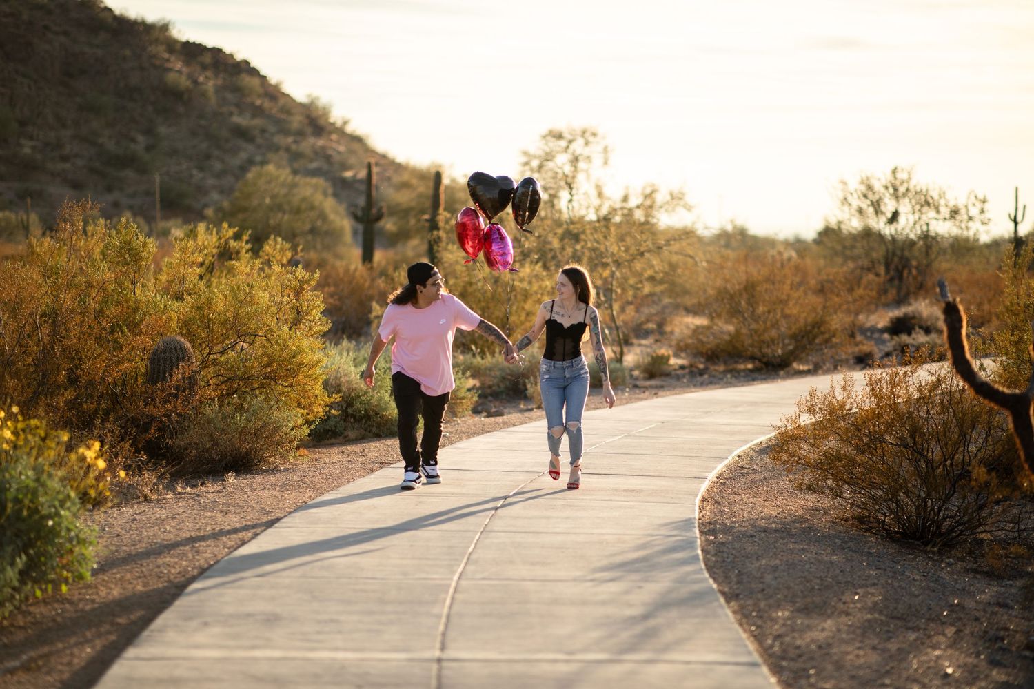 People walking on a winding desert trail surrounded by desert brush and cacti during golden hour at Desert Arroyo Park in Mesa, Arizona.