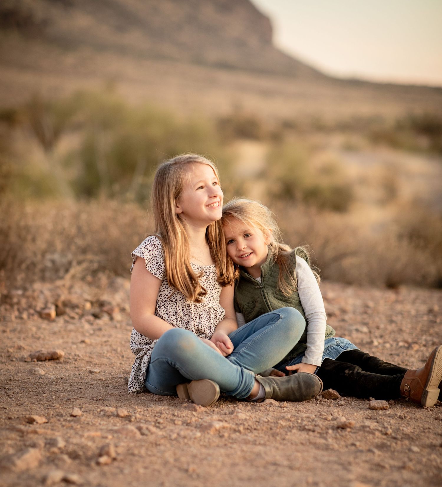 Two people share a tender moment while laying on desert ground at sunset at Lost Dutchman state park.