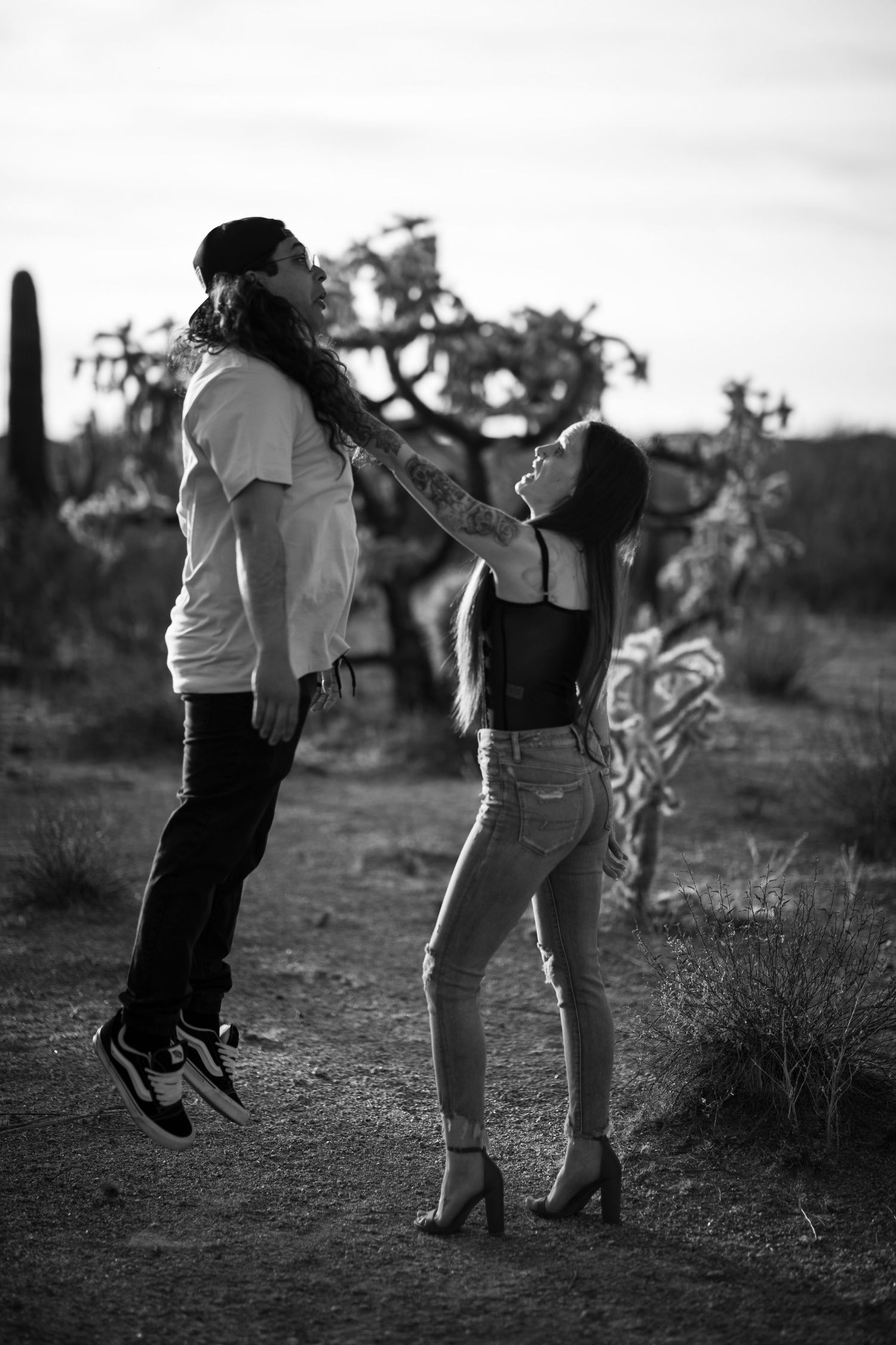 A black and white photo sequence shows two people playfully jumping together at Desert Arroyo Park in Mesa, Arizona.