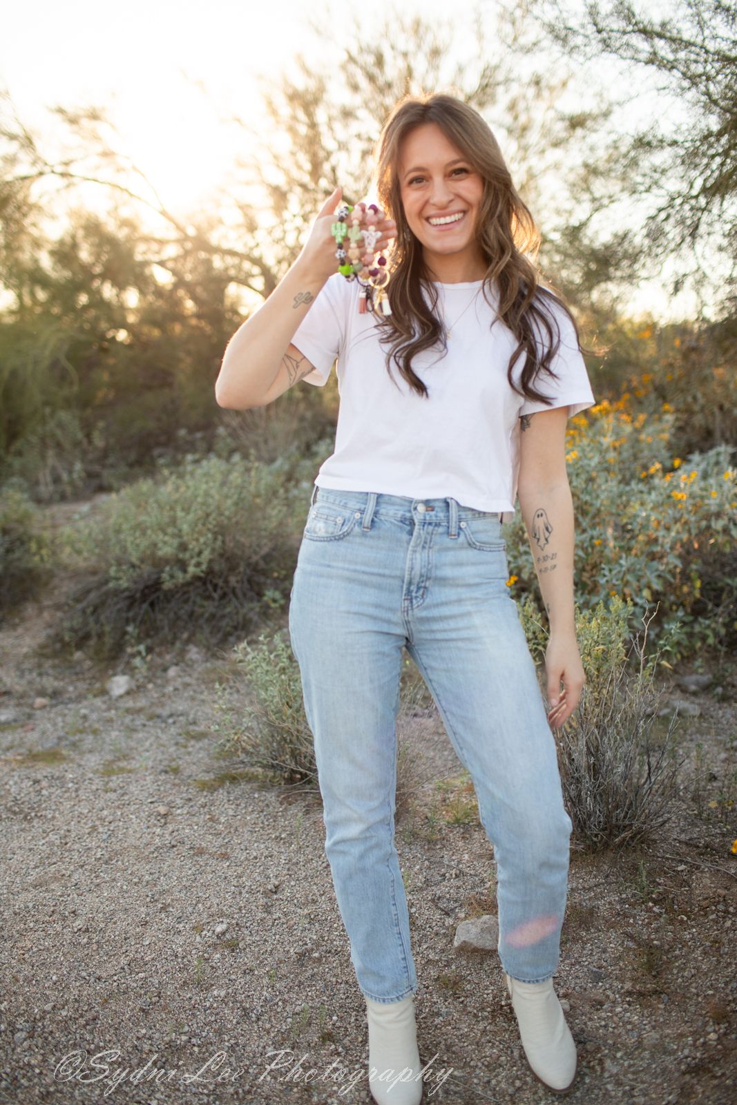 Person wearing light blue mom jeans and white sneakers poses in a desert landscape with wildflowers at sunset.
