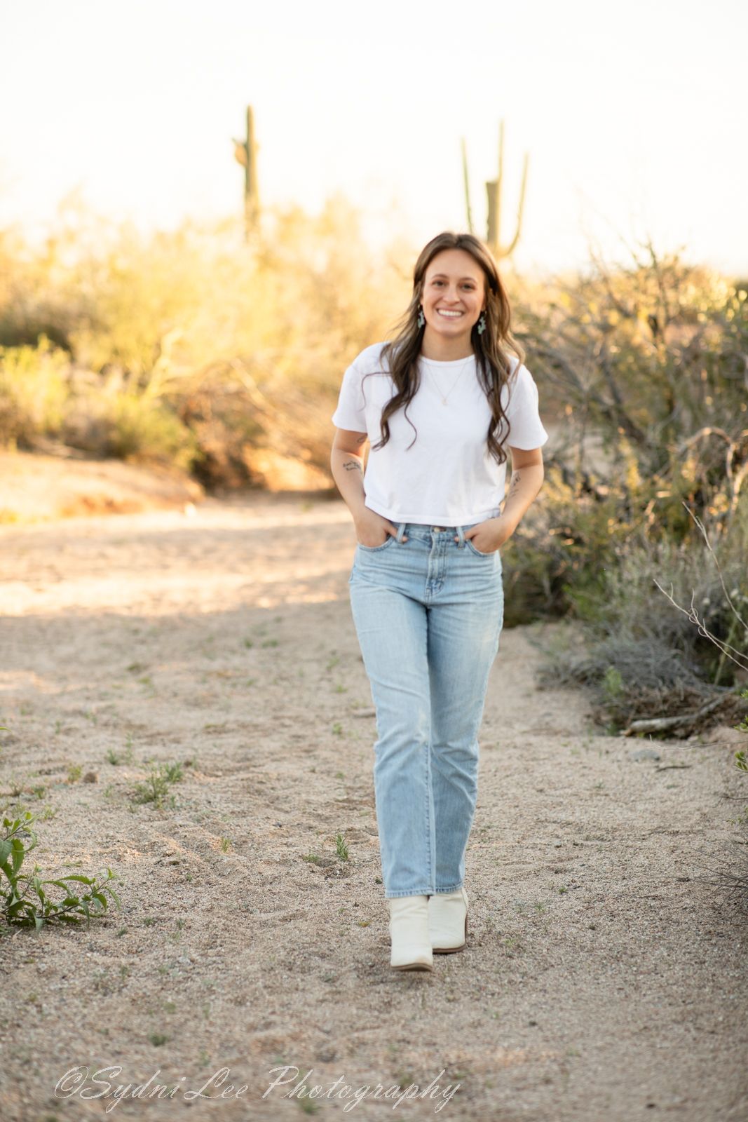 A desert photoshoot featuring casual denim and white boots with cacti in the background.