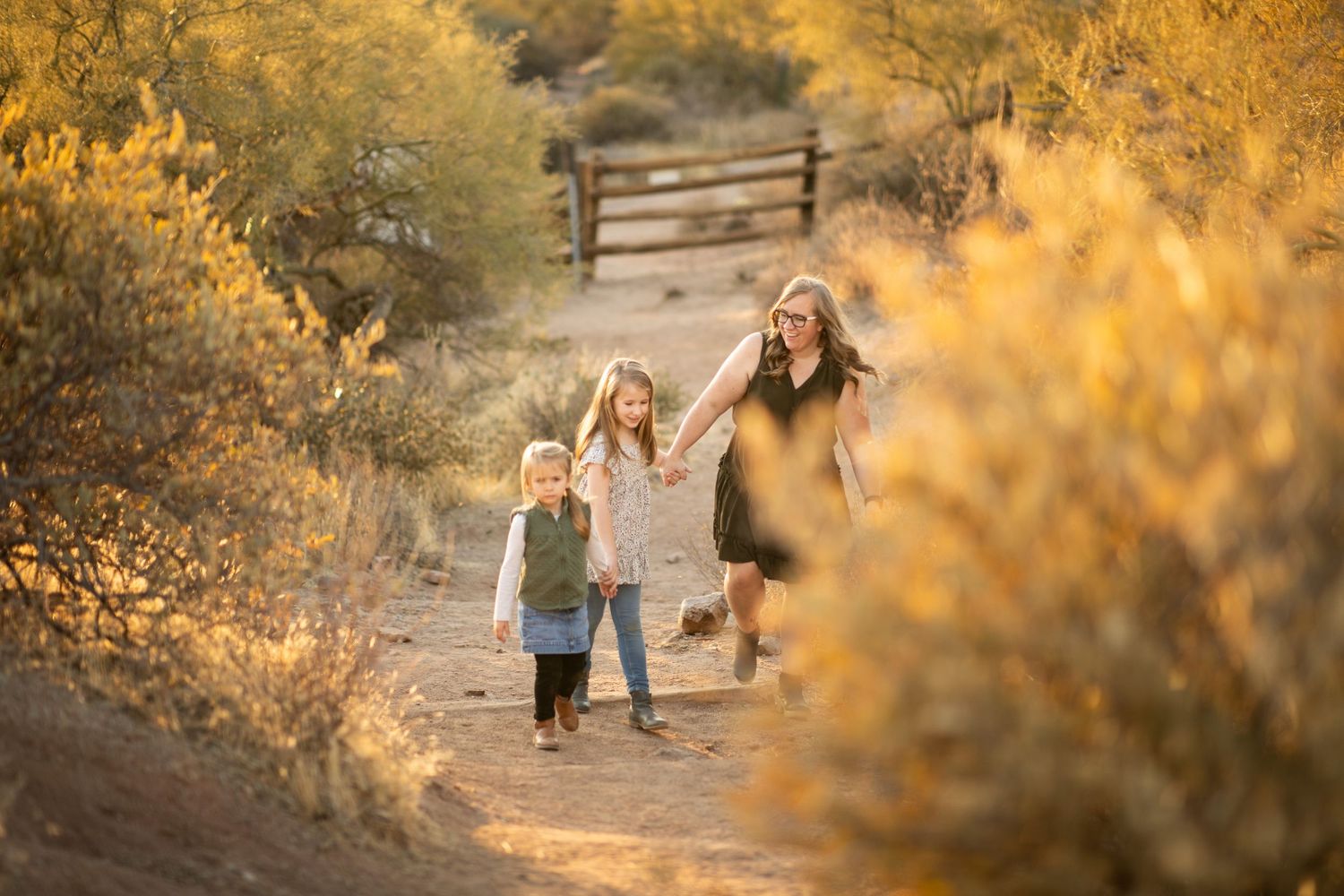 Golden sunlit desert landscape with figures walking along winding dirt paths during a warm autumn evening at Lost Dutchman state park.