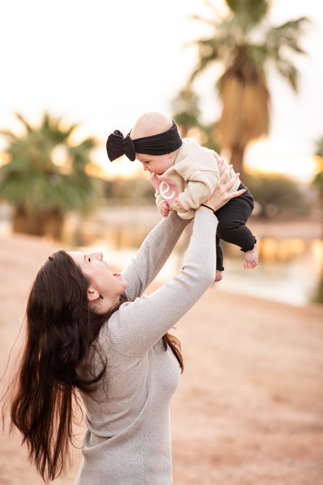 A heartwarming moment captured outdoors with a baby being lifted up against a backdrop of palm trees at sunset in Papago Park in Phoenix, AZ