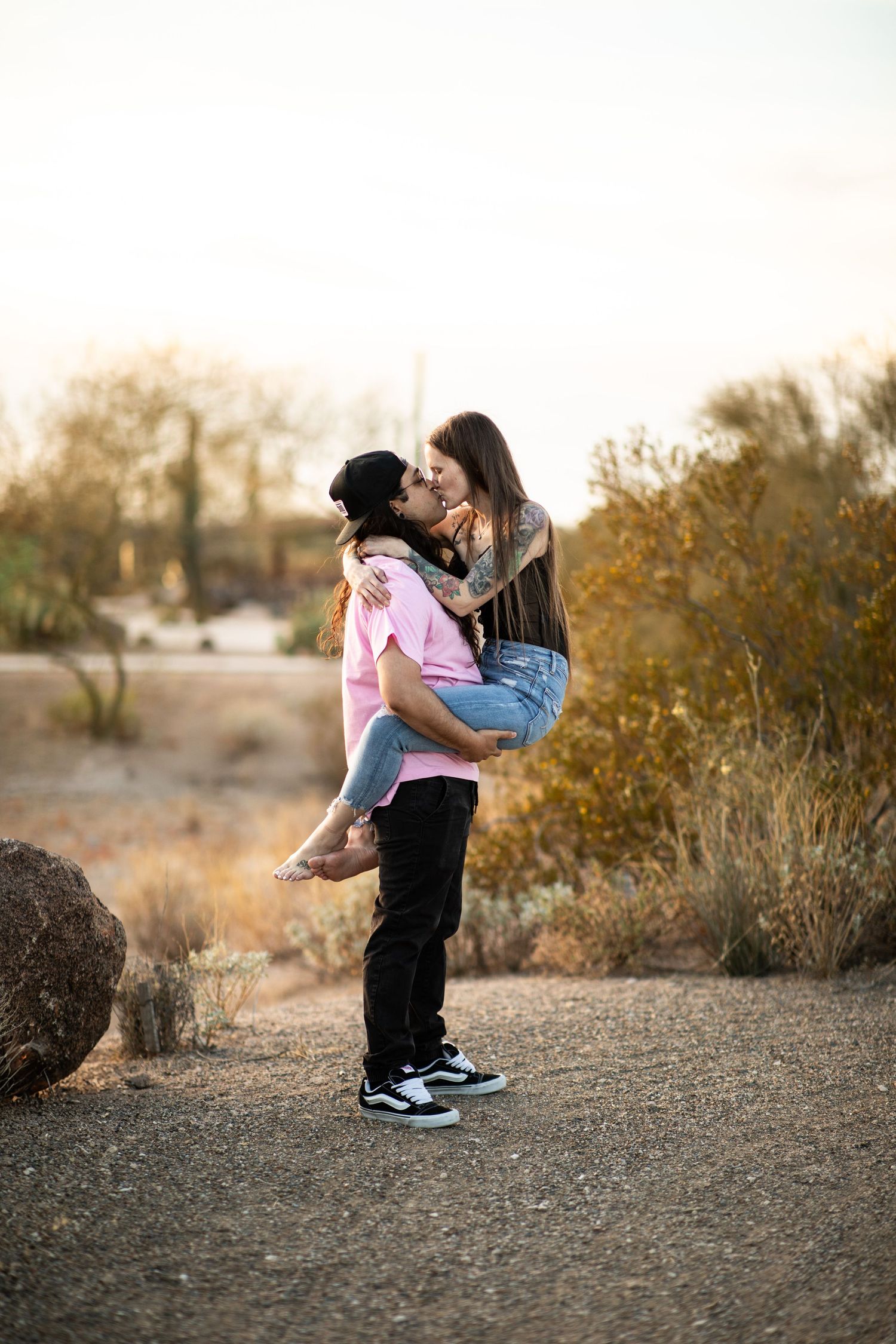 A couple embraces playfully in a desert setting during golden hour, creating silhouettes against the fading light at Desert Arroyo Park.