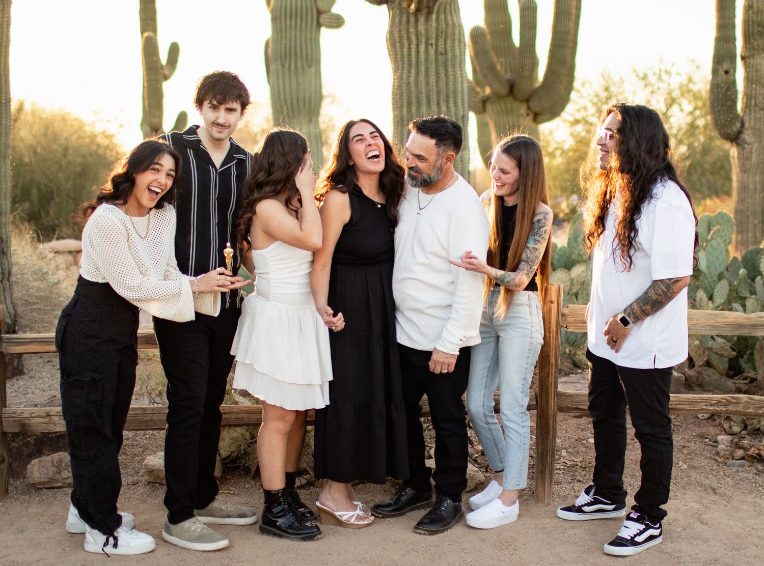 Group of friends laughing together in casual attire against backdrop of tall desert cactus at sunset.