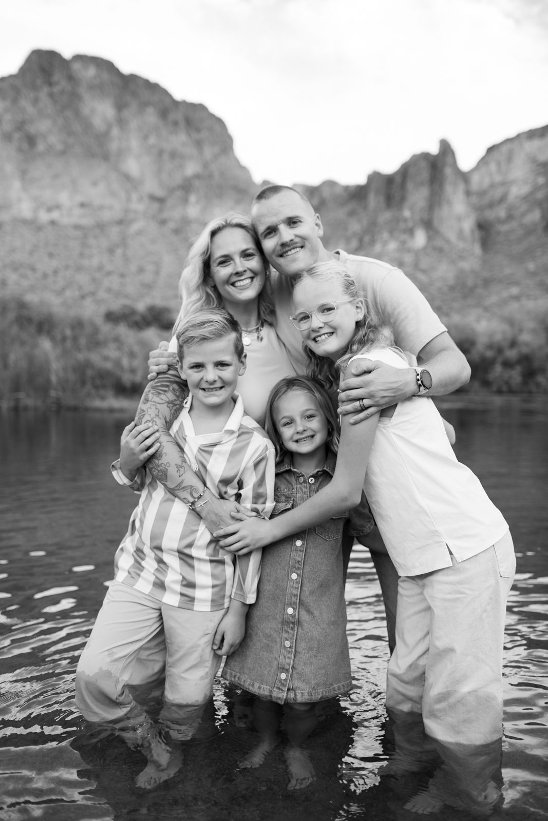 Family embracing while standing in water with dramatic mountain scenery behind them at Water Users recreational area.