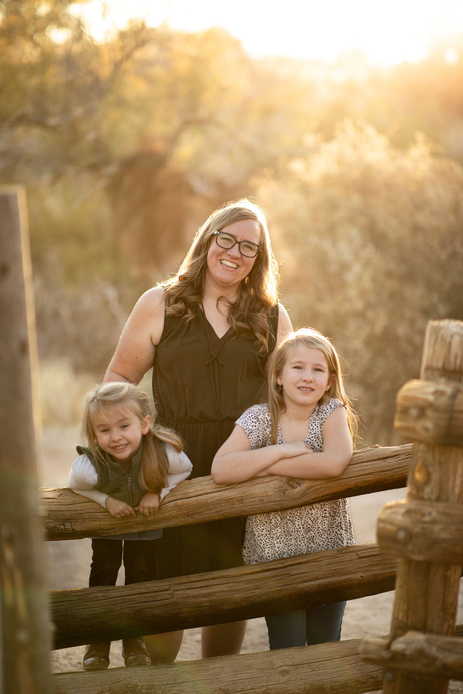 Family members share joyful laughter while leaning on a rustic wooden fence during golden hour sunset at Lost Dutchman State Park.