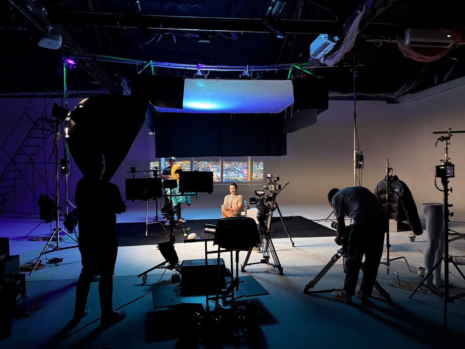 Behind the scenes view of a film production studio with silhouetted crew members and lighting equipment.