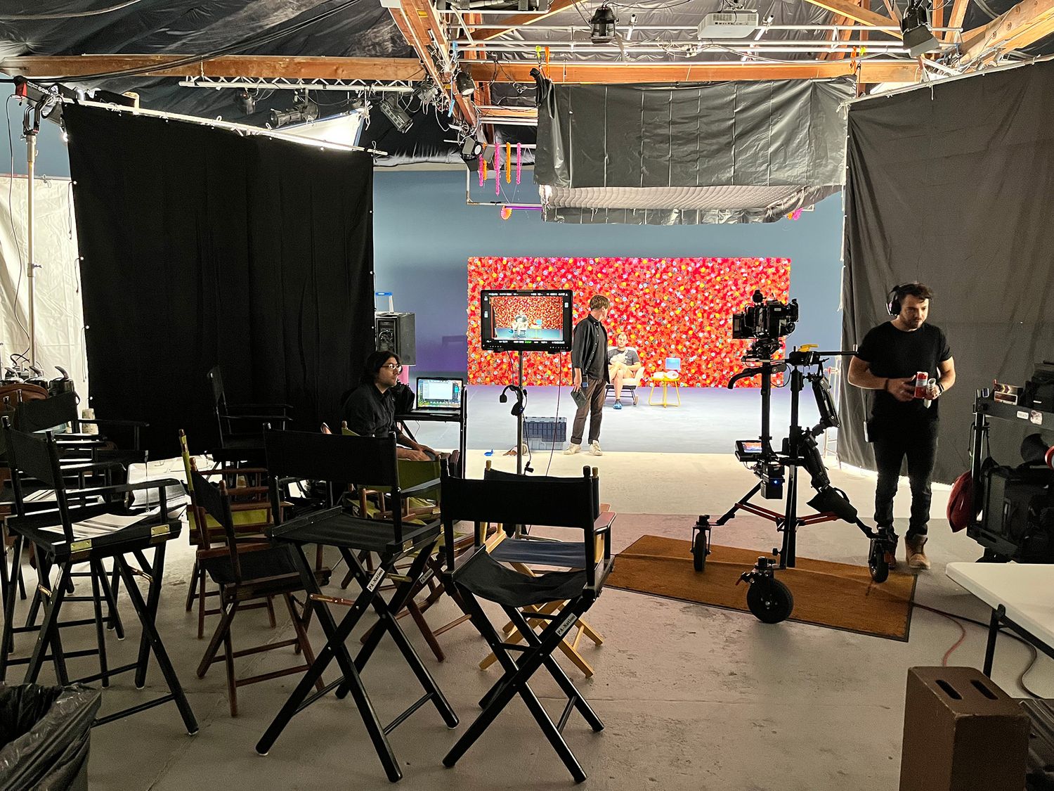 Behind the scenes view of a video production set with black director chairs and lighting equipment in a studio.