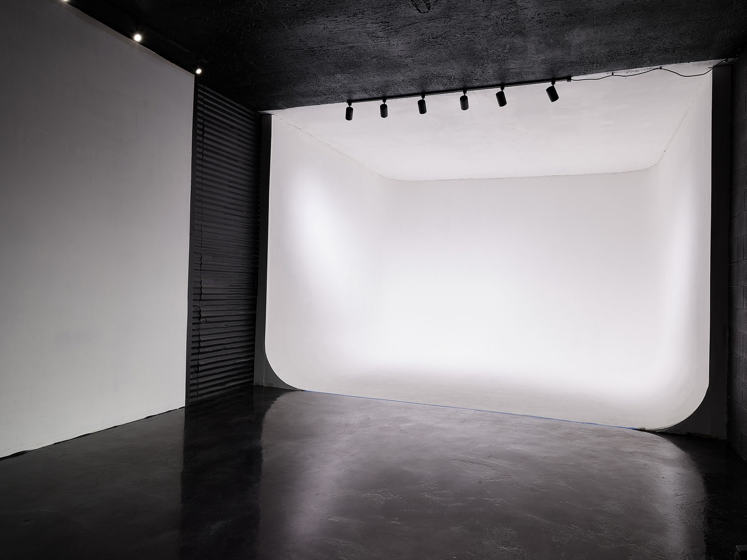 Empty white photography studio with seamless backdrop and track lighting mounted on black ceiling.