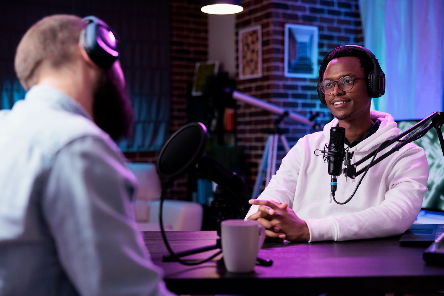 A person speaks into a microphone in a studio setting with purple and blue lighting.