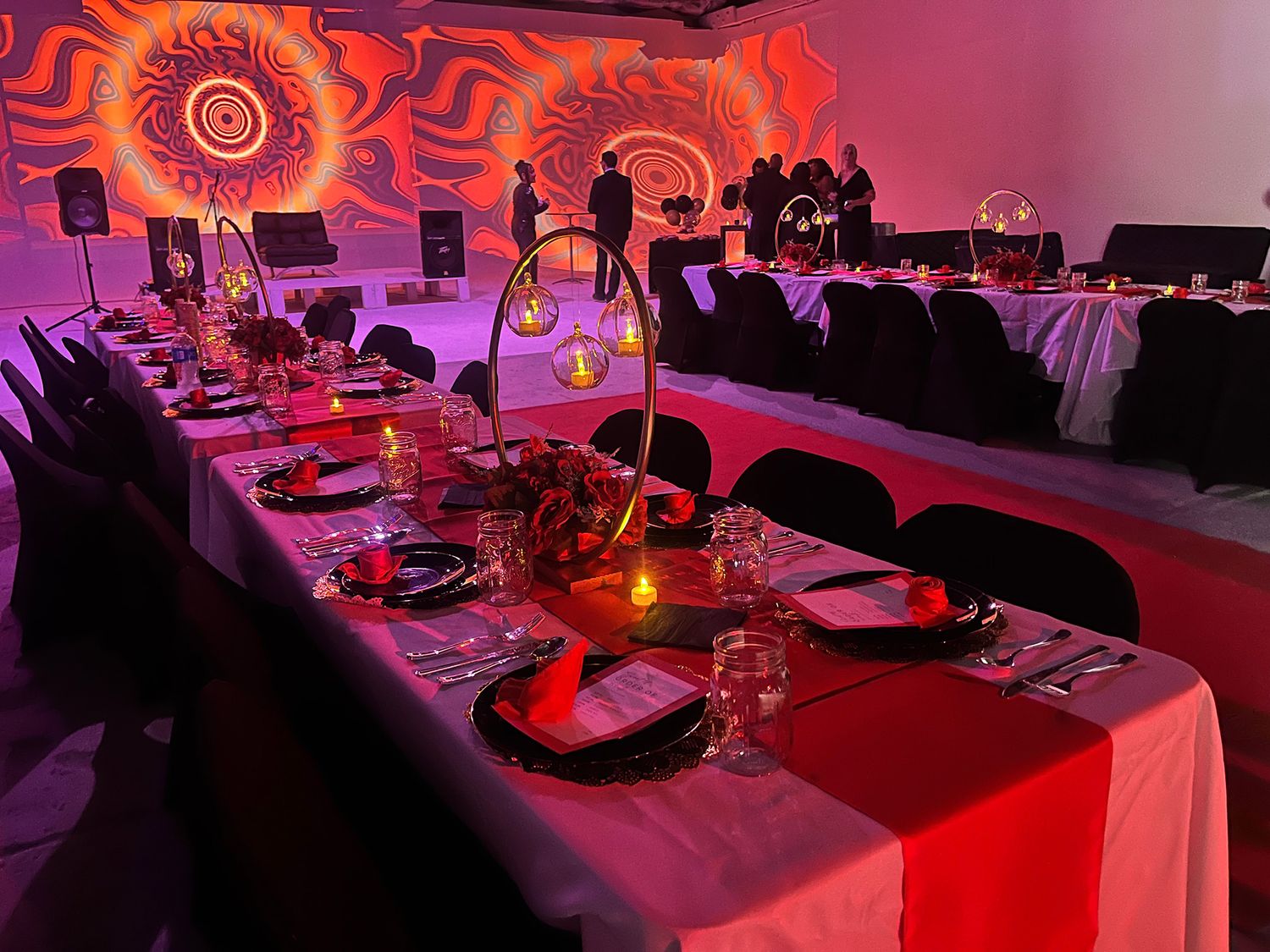 Elegant banquet tables with red and pink uplighting create a dramatic atmosphere for an upscale event setup.