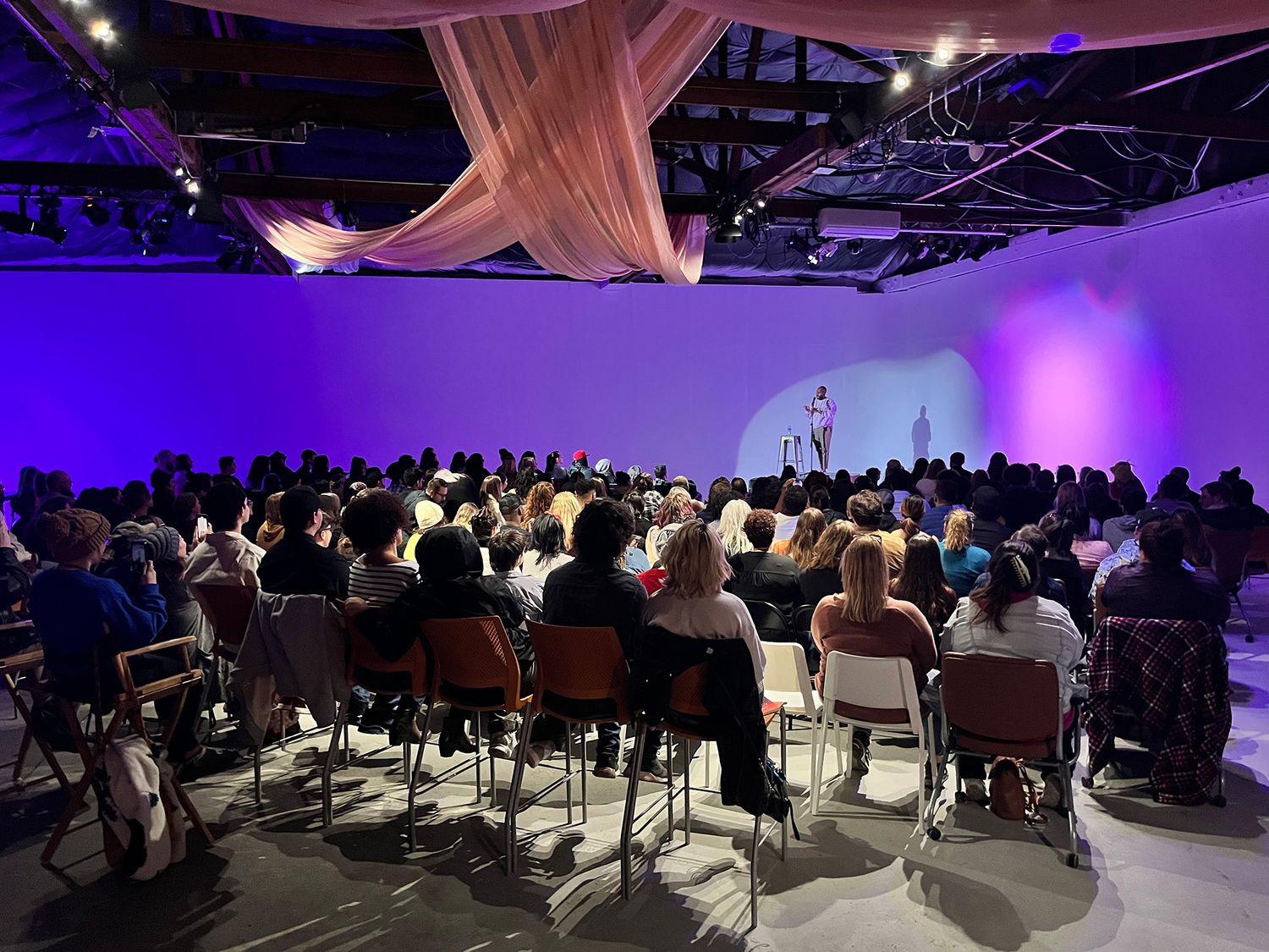 Large audience seated in a dimly lit auditorium with purple ambient lighting.