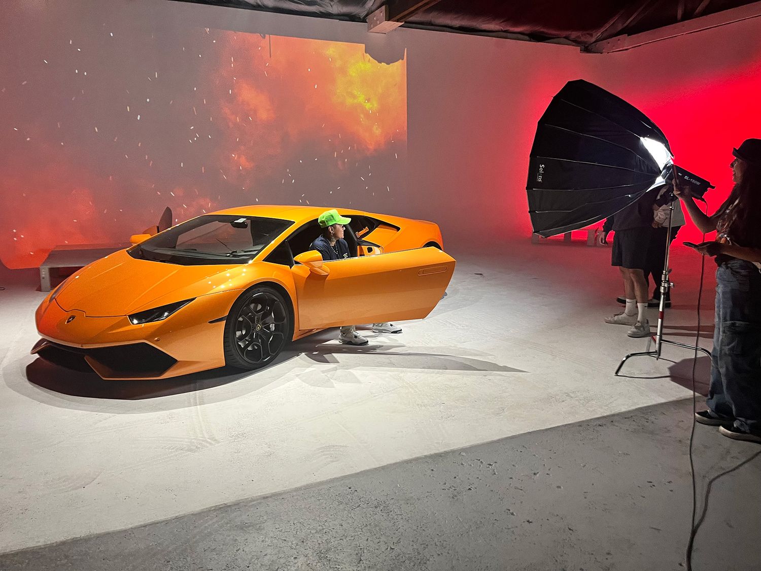 Yellow sports car on display in a studio with dramatic red lighting and professional photography equipment.