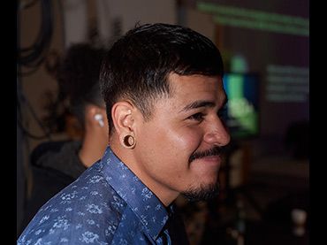 Profile view in dimly lit indoor setting with blue patterned shirt.