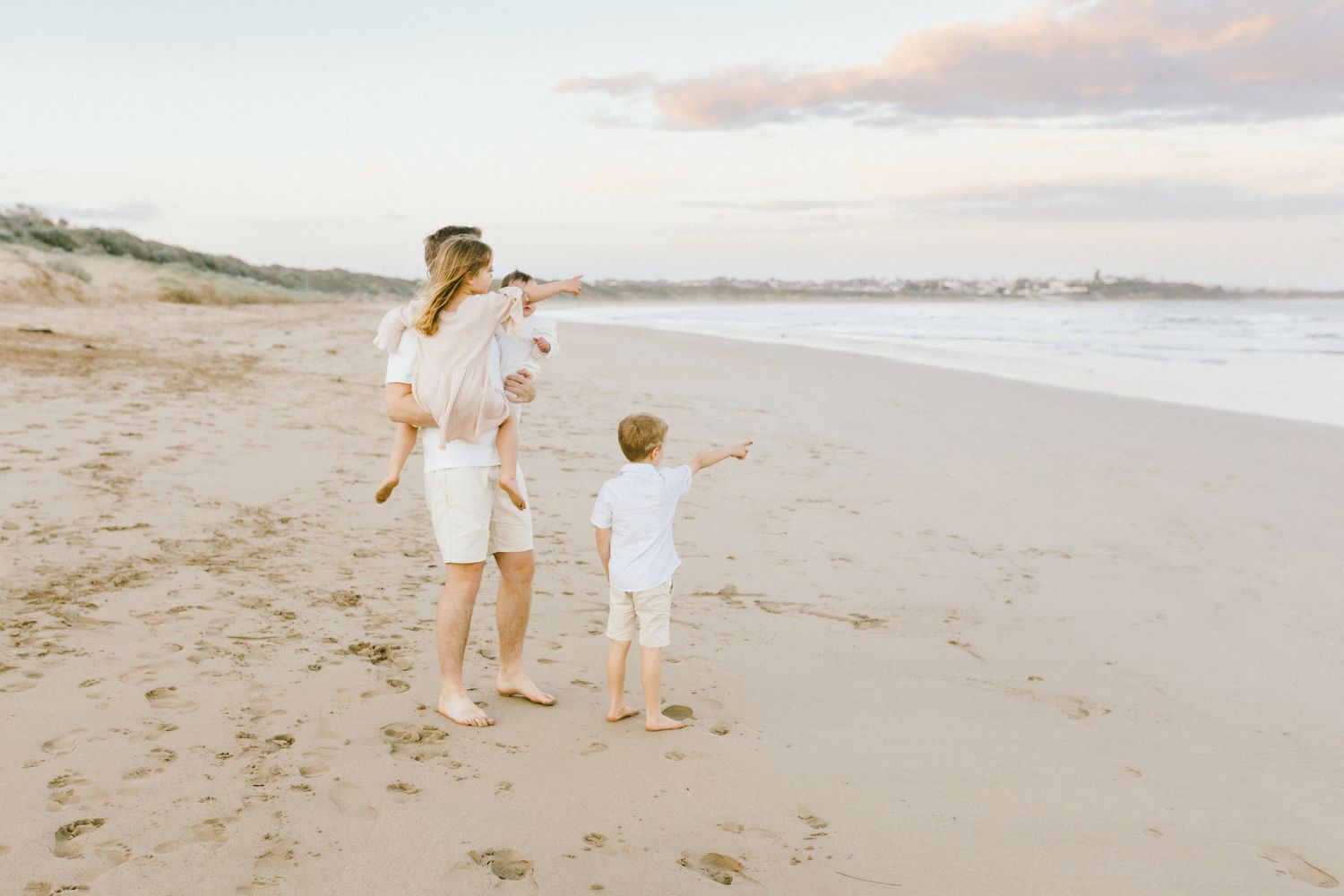 Family members walk together along a peaceful sandy beach at sunset, enjoying quality time by the ocean.