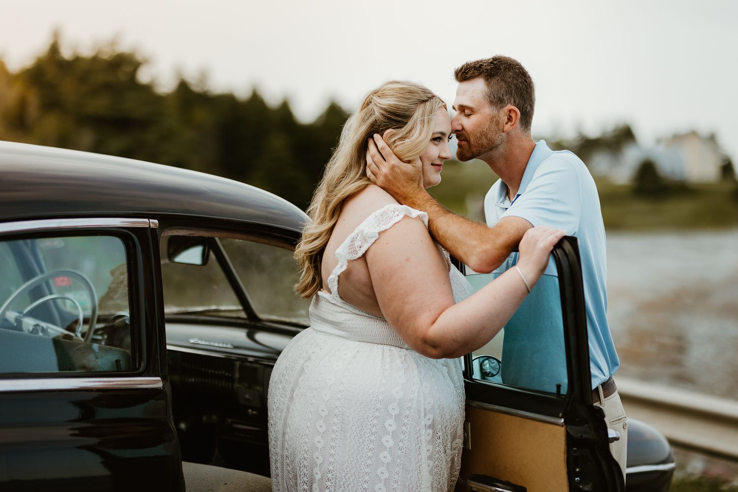 Romantic photoshoot featuring a vintage car and natural outdoor backdrop at sunset.