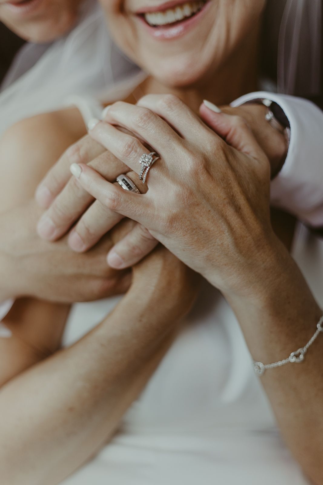 Close-up of hands showing wedding rings and jewelry in an intimate moment.