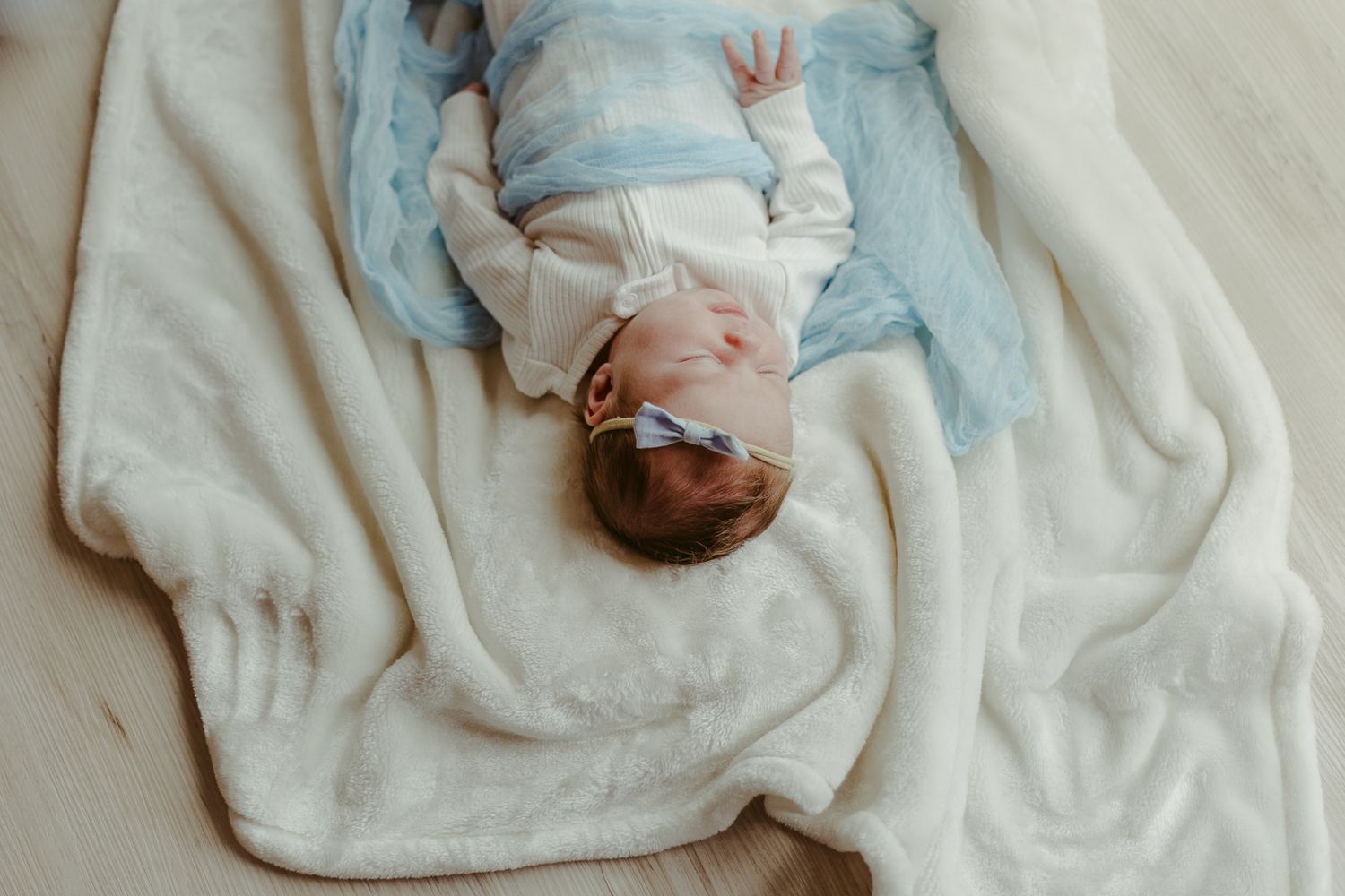 Newborn baby sleeping peacefully on soft white and blue blankets.