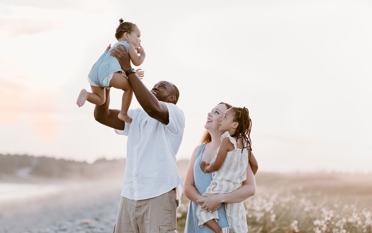Family playing and lifting child in air during sunset beach photoshoot.