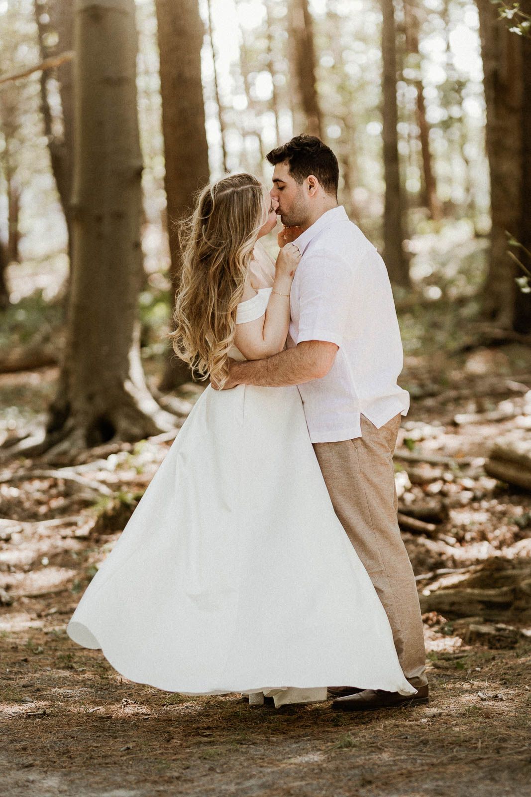 A couple shares intimate moments during their forest wedding photoshoot with sunlight filtering through trees.
