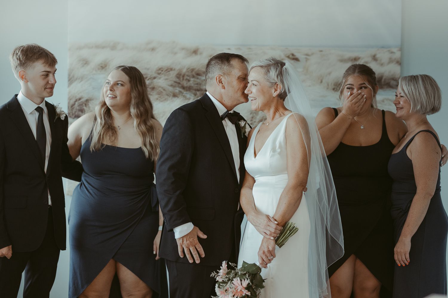 Wedding party poses together in formal attire with the couple at center.