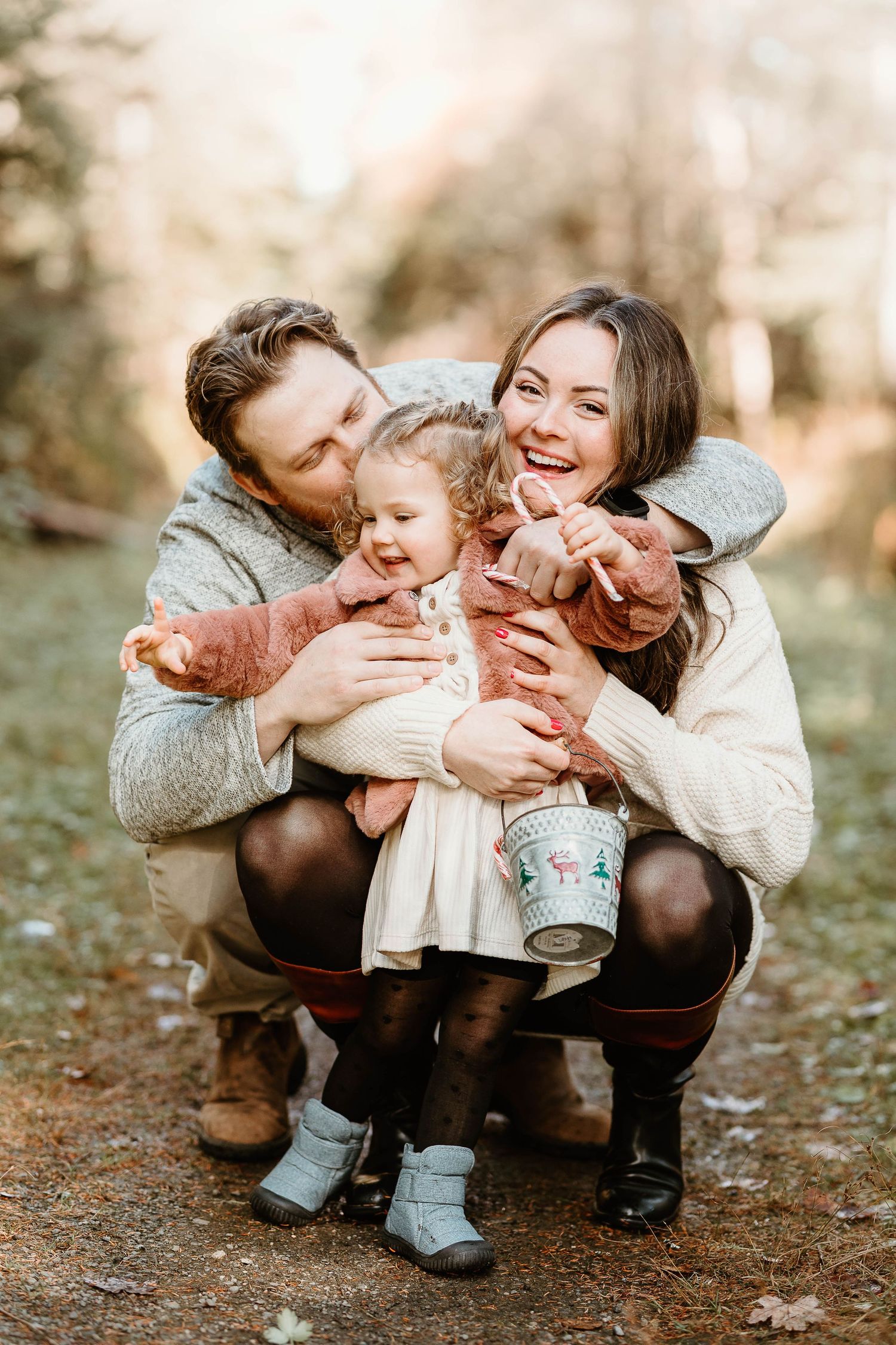 Happy family of three sharing a joyful moment outdoors in autumn, parents hugging their toddler daughter in a forest.