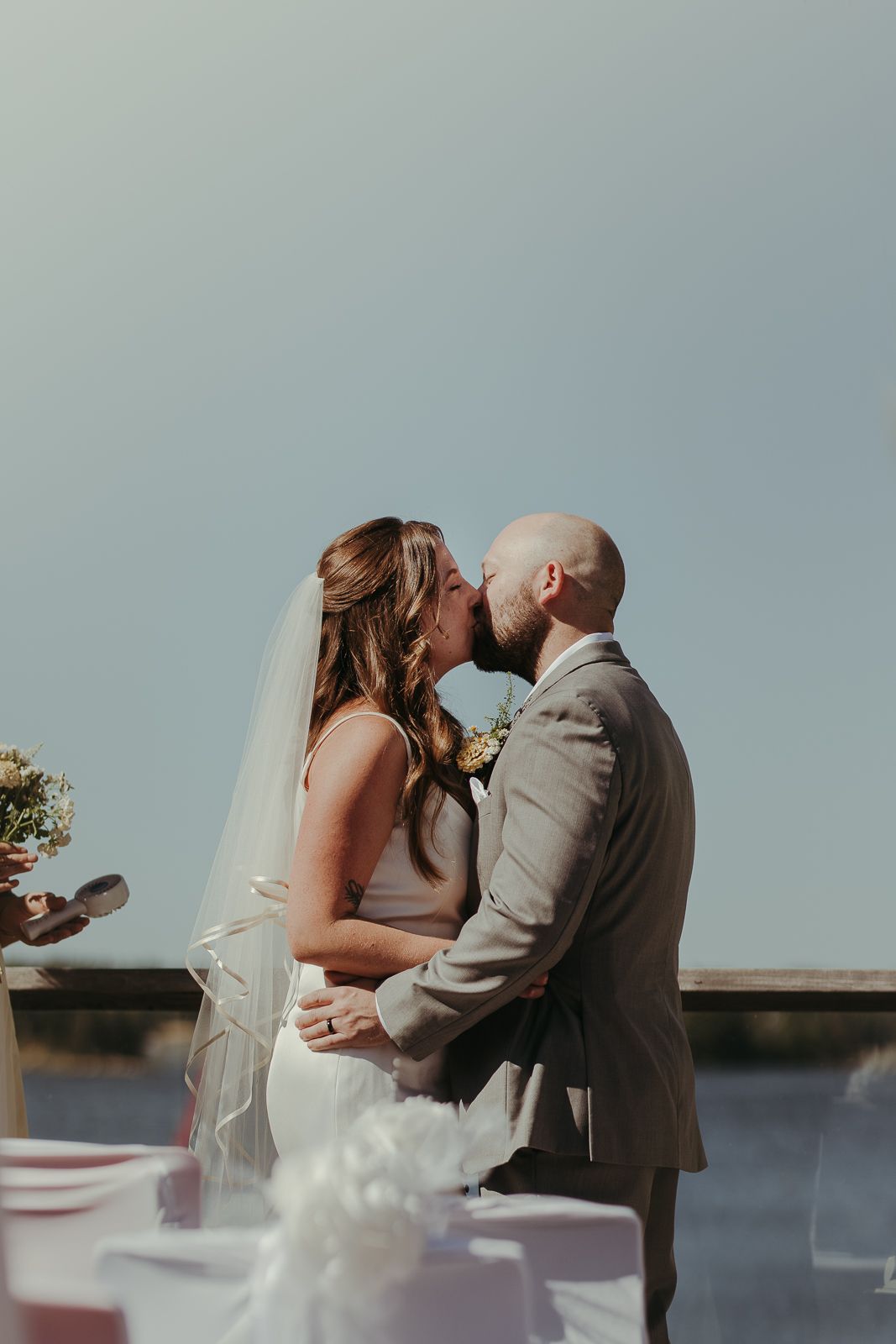 Sequence of romantic wedding kiss photos captured against soft blue sky at outdoor ceremony.
