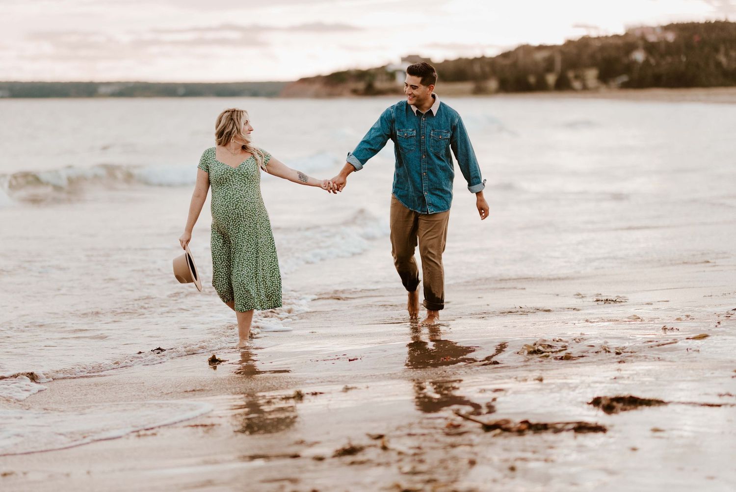 Couple holding hands walking along a sandy beach shore with gentle waves, wearing casual summer outfits.