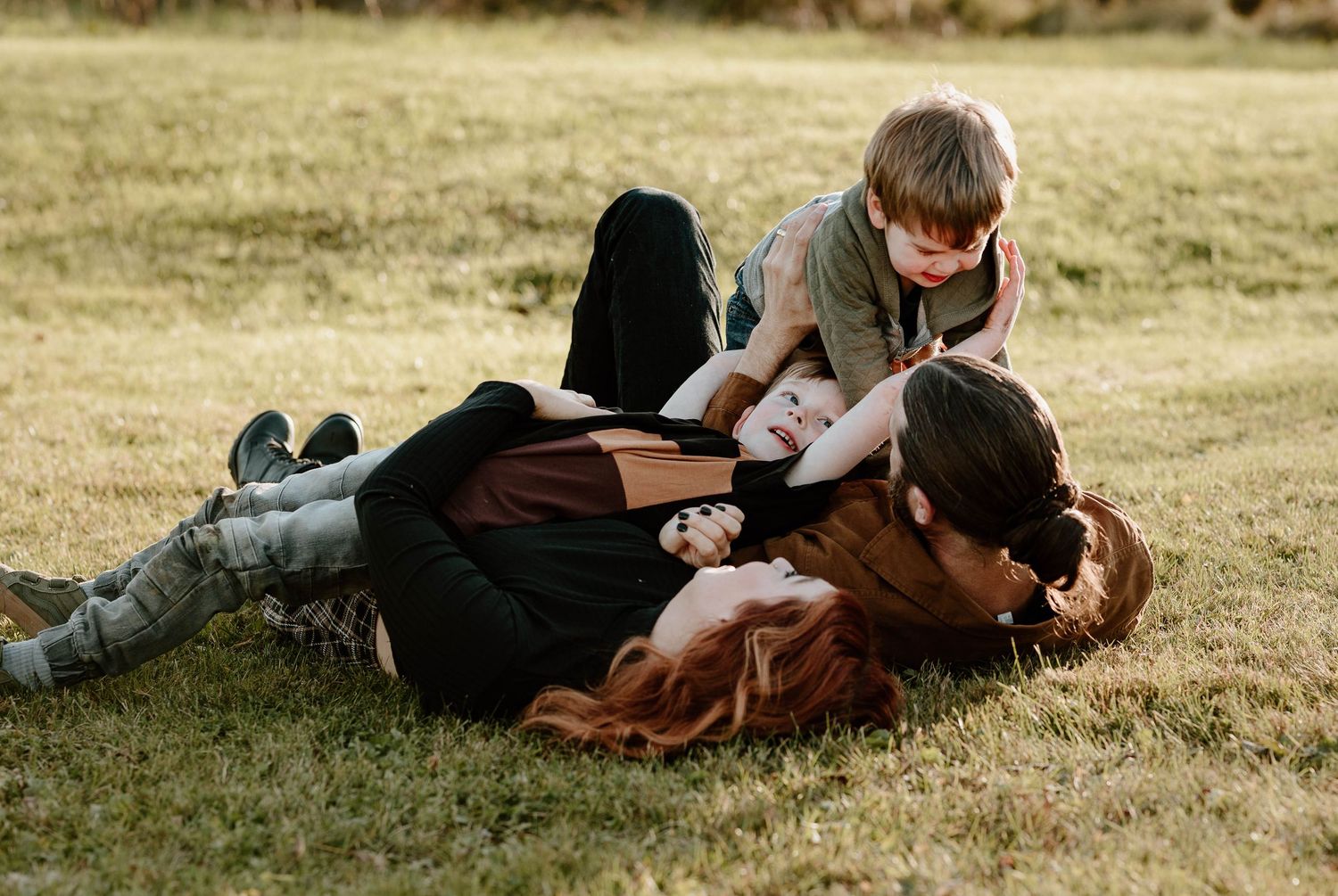 Family lying together on grass during golden hour outdoor photo session.