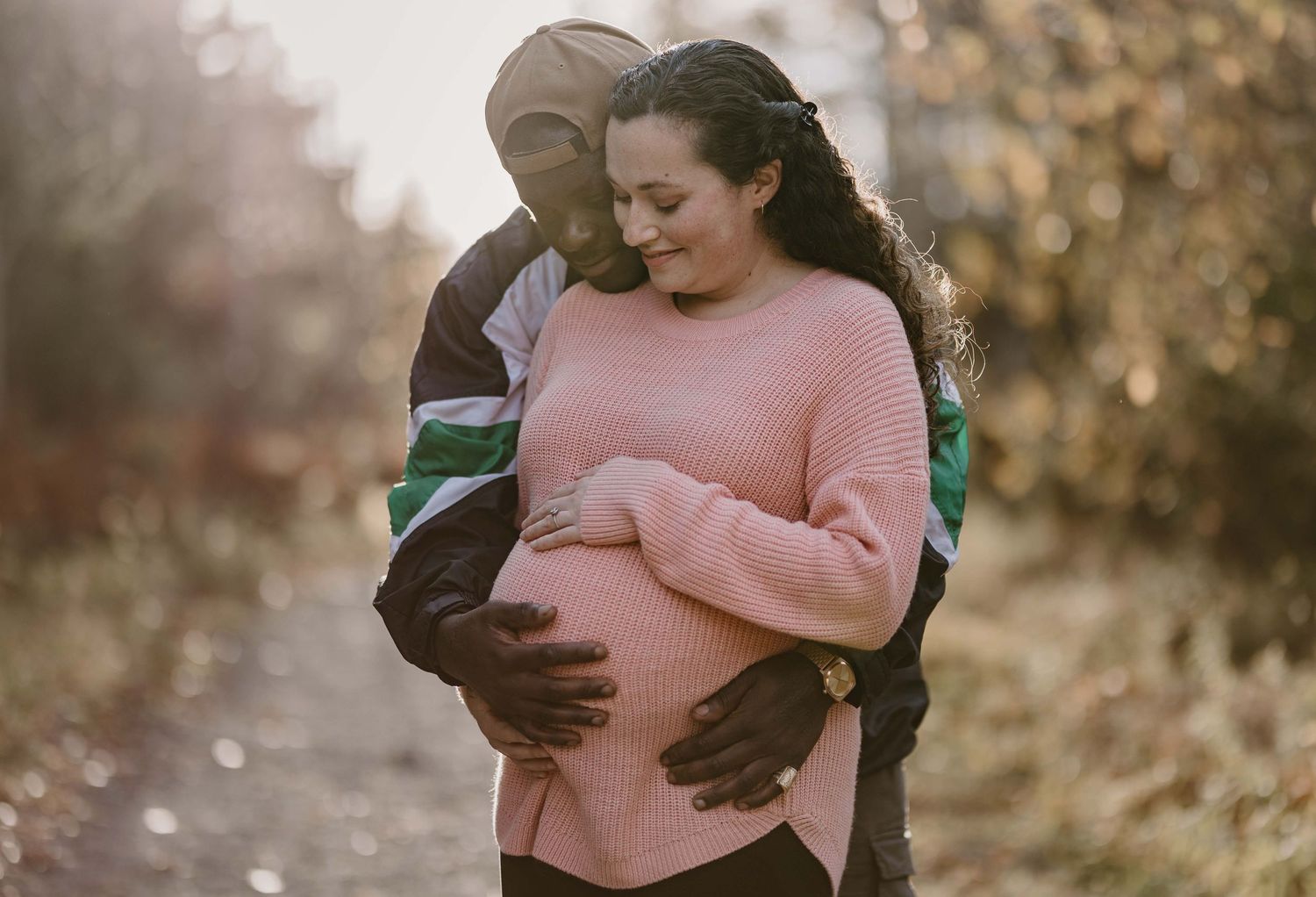 Romantic outdoor maternity photo shoot with couple embracing in fall setting.