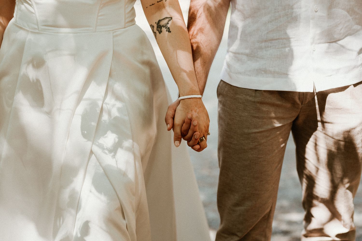 Close-up shot of couple holding hands while wearing white and casual wedding attire.