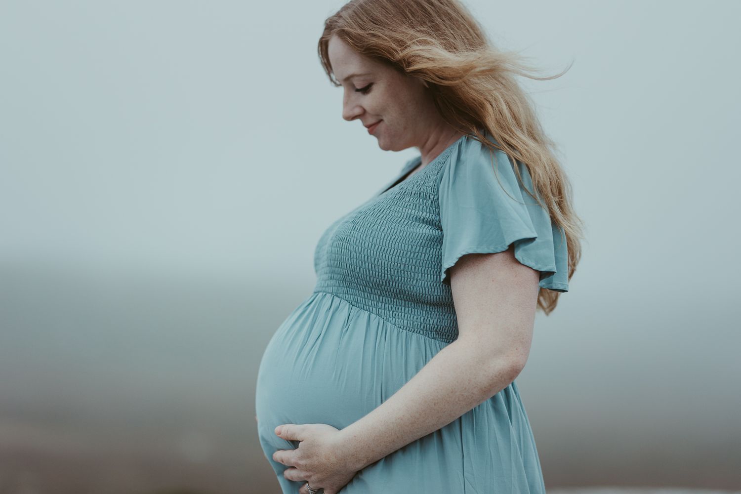 Maternity photo showing woman in blue dress against light background.