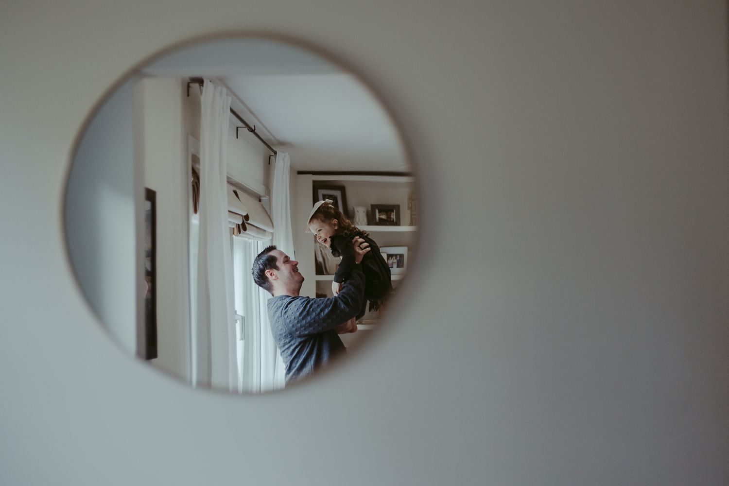 Mirror reflections in an oval frame showing glimpses of a father holding his daughter.