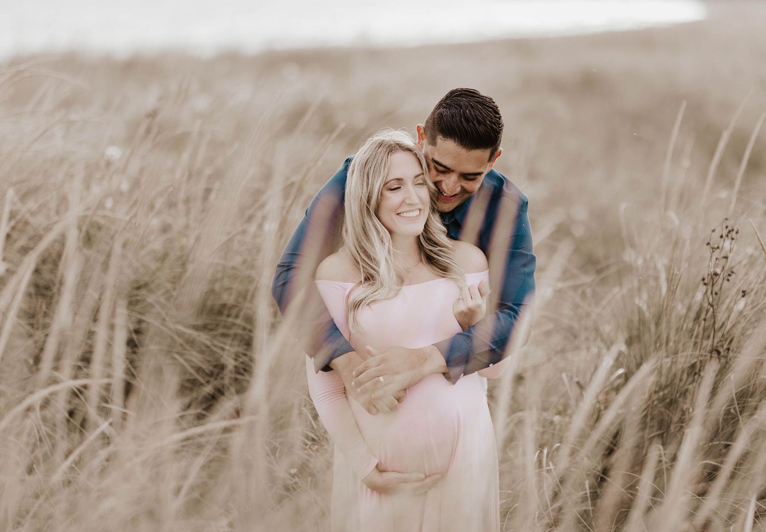 Romantic maternity photos in tall grass field at golden hour.