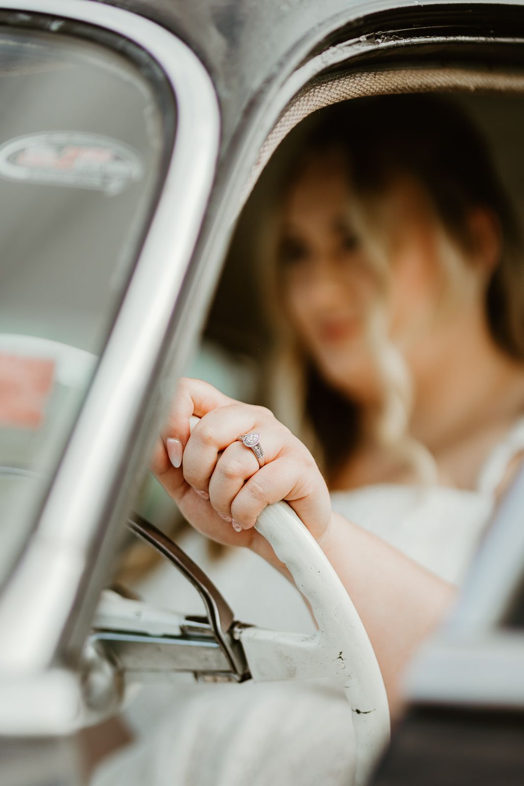Close-up detail shot of hand wearing engagement ring inside vintage car.