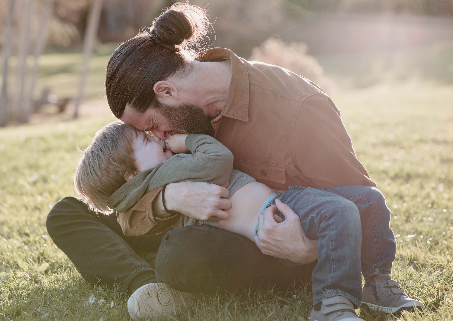 Candid family moments captured while sitting together on grassy hill during sunset.