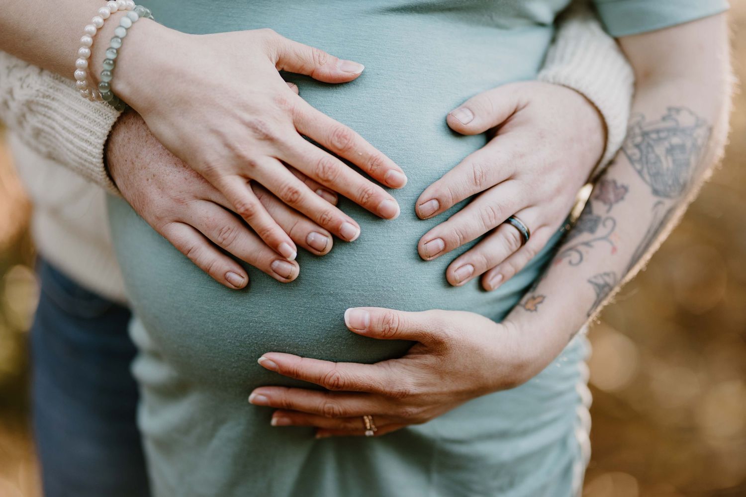 Detail shot of hands cradling pregnant belly in mint green maternity dress.