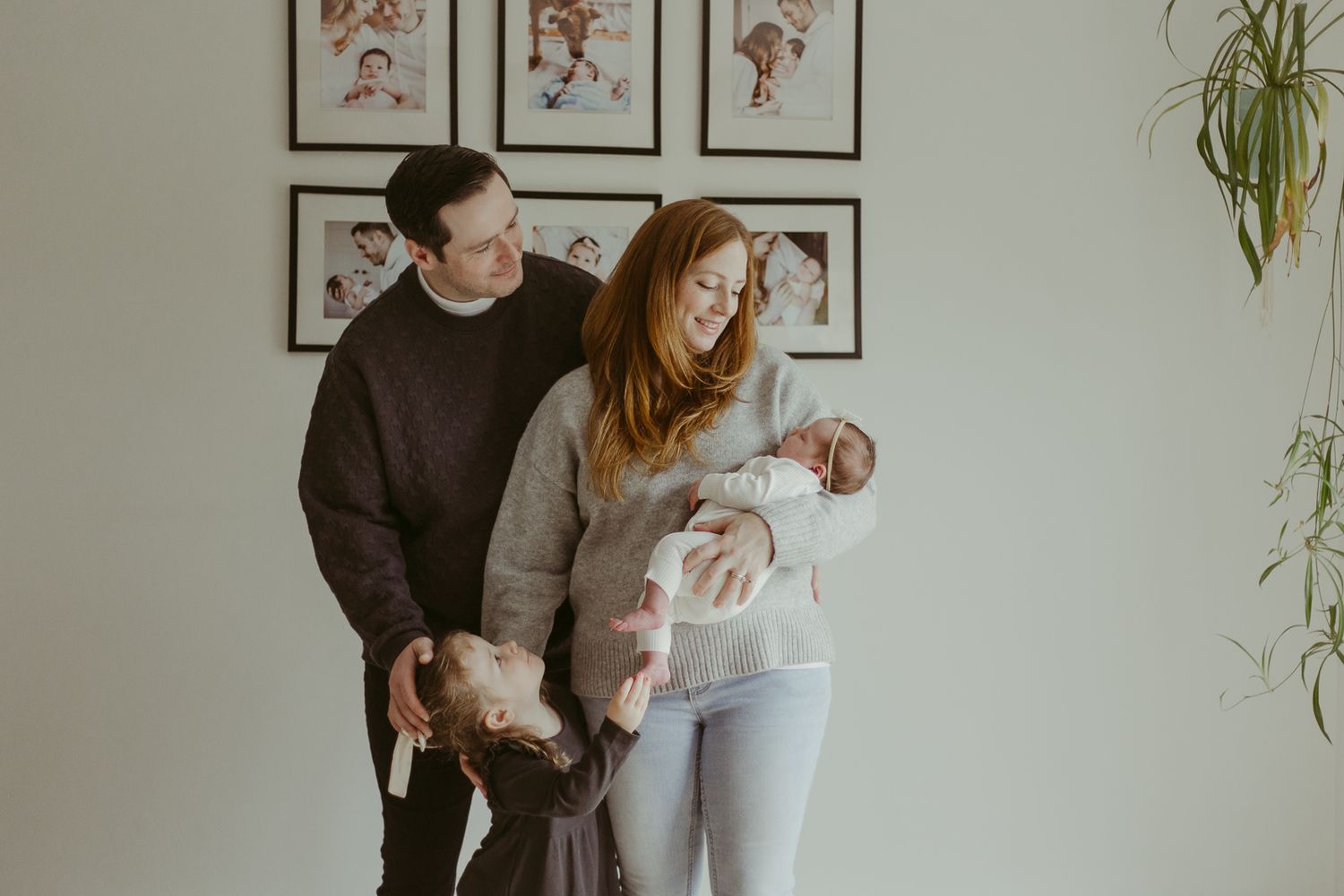 Family gathering with newborn in front of prior family photos in home.